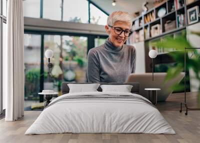 Portrait of a cheerful mature businesswoman working on laptop at home office. Wall mural