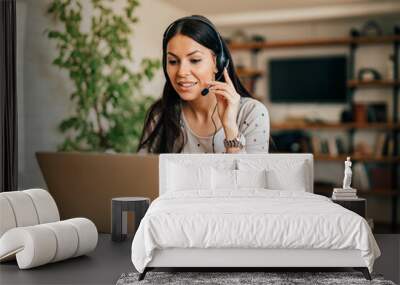 Portrait of a cute woman with headset and laptop at home office. Wall mural