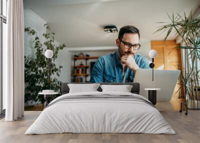 Portrait of a handsome man using laptop at home. Wall mural