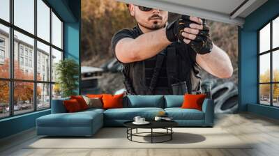 Portrait of a heavily armed young man shooting a gun outdoors.Special forces soldier on a practice. Wall mural