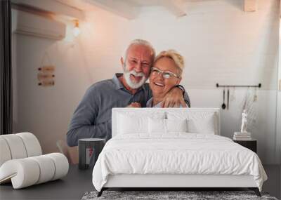 Portrait of a loving senior couple indoors. Hugging, smiling and looking at camera. Wall mural