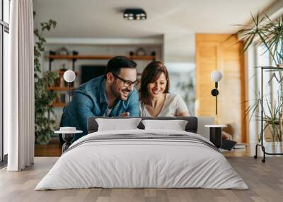 Portrait of a smiling couple looking at laptop together at cozy home office. Wall mural