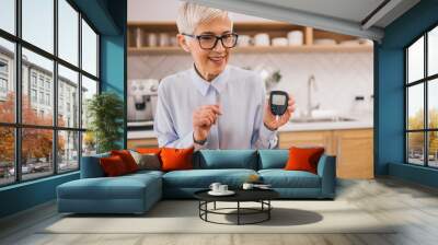 Portrait of a smiling woman having online meeting, showing glucose meter. Wall mural