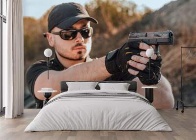 Portrait of a young man shooting a hand gun outdoors, close-up. Wall mural