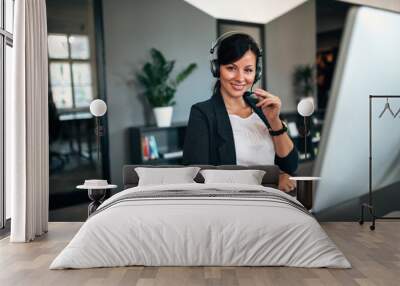 Portrait of beautiful businesswoman working with headset as a customer support, looking at the camera. Wall mural