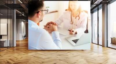 Portrait of female doctor sitting at desk with young patient while check up and write diagnosis. Wall mural