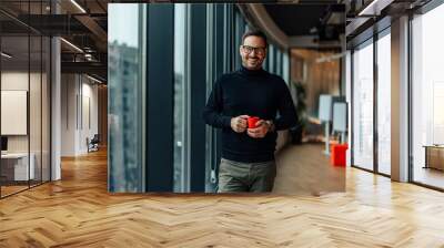 Portrait of happy adult man, holding a cup of tea and smiling near the window. Wall mural