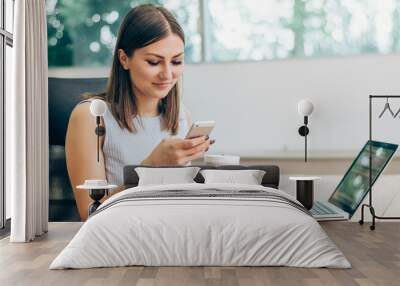 Portrait of smiling modern business woman in office using her mobile phone. Wall mural