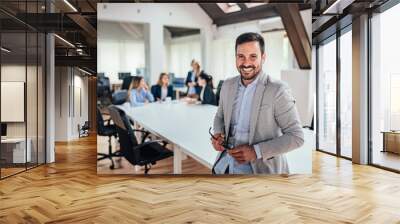 Portrait of successful entrepreneur, colleagues working in the background. Wall mural