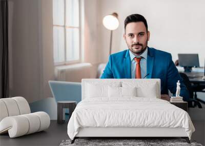 Portrait of young smiling businessman with laptop sitting in modern office. Wall mural