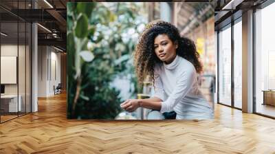 Portrait of young woman with curly afro hair standing against fence in shopping mall. Wall mural