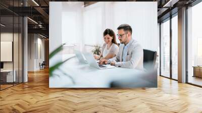 Positive adult business man and woman colleagues sitting with laptops on desk in office Wall mural