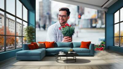 Positive young man buying flowers outdoors. Wall mural