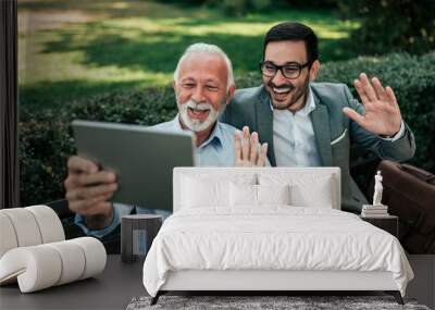 Senior father and adult son having a video call outdoors. Wall mural