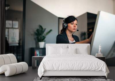 Serious businesswoman with headset solving problems while working on computer in modern office. Wall mural