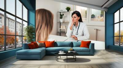 Serious female doctor listening to a patient. Wall mural