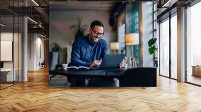 Smiling adult man typing something over the laptop, working online. Wall mural