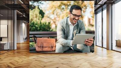 Smiling business man using tablet while sitting on the bench. Wall mural