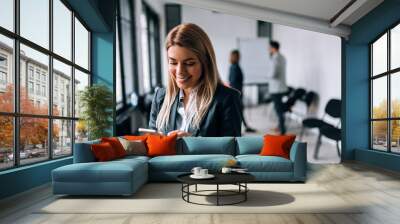 Smiling business woman using phone during a break. Collegues standing in the background Wall mural