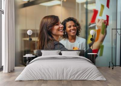 Smiling businesswoman brainstorming with adhesive notes on a glass wall in the office. Wall mural