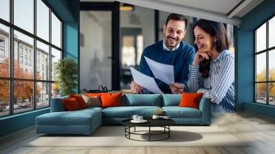 Smiling caucasina man, showing the documents to his female coworker. Wall mural