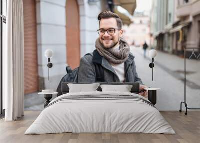 Smiling young man with smartphone in  the city with backpack wearing winter clothes. Wall mural