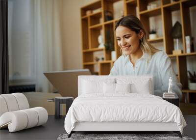 Smiling young woman using laptop at home, portrait. Wall mural