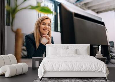 Sucessful smiling businesswoman sitting at the office in front of a computer. Wall mural