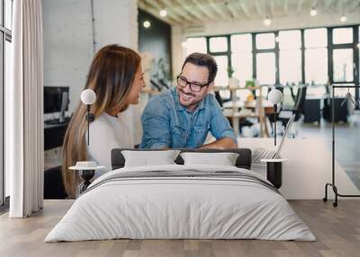 Two cheerful colleagues smiling while discussing something in modern office. Wall mural