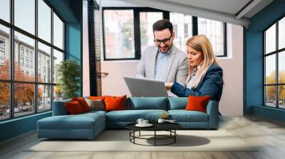 Young business man holding a laptop while discussing new project with his female collegue Wall mural