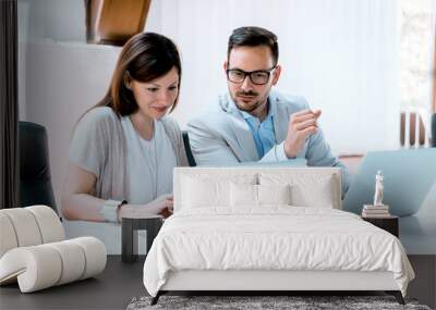 Young businessman discussing with his female colleague, and using a lap top in the office. Wall mural