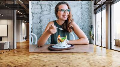 Young cheerful woman eating fruit salad. Wall mural