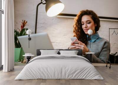 Young entrepreneur at her workplace using laptop and phone. Wall mural