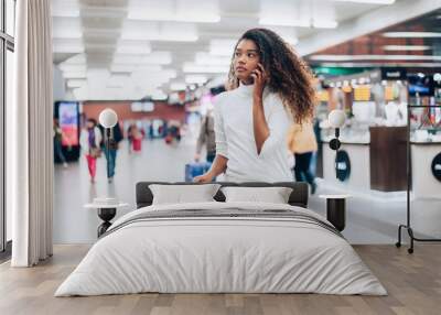 Young woman at the airport with trolley bag, talking on the phone. Wall mural