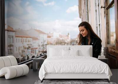 Young woman working on a balcony. Using smartphone and laptop computer outdoors. Wall mural