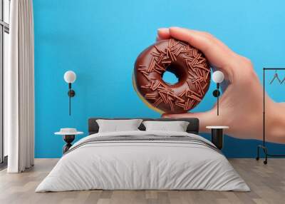 Chocolate donut in hand on blue background Wall mural