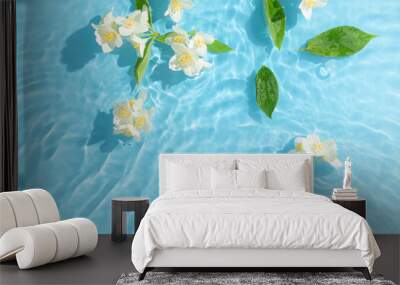 Jasmine flowers and leaves floating on bright blue wavy water. Minimal nature background. Summer scene with sunny day shadows. Wall mural