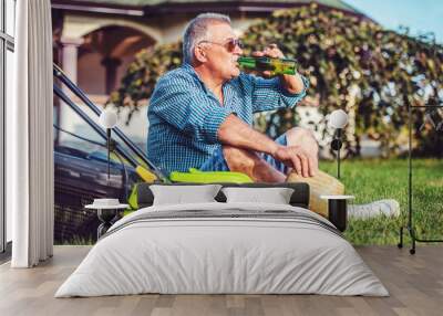 Gardening. Senior man take a rest in the yard and enjoying in beer after work with a lawn mower. Hobbies and leisure Wall mural