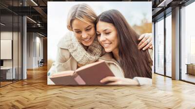 Two young women reading a book in the park Wall mural