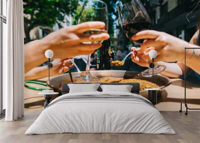 two girls holding drinks wine start eating paella with seafood and squid at a table in a restaurant Wall mural