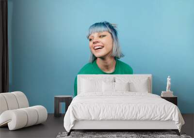 Attractive lady with colored hair with a smile on her face isolated on a blue background in a green sweater looking aside Wall mural