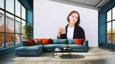 Attractive young woman wearing a suit standing on a white background with a glass of coffee in her hands and looking into the camera. Copyspace Wall mural