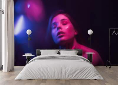 Background. Blurred abstract photo of a woman with glitter on her face dancing out of focus in a dark room with purple and blue light. Wall mural