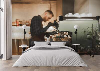 Bearded man barista steaming milk on a professional coffee machine. Process of cooking coffee on a coffee machine in the coffee shop. Focus on coffee machine. Background. Copyspace Wall mural