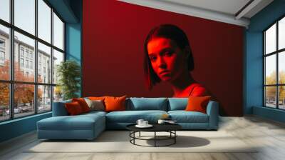 Close fashion portrait of attractive woman in red neon light on wall background, posing at camera. Wall mural