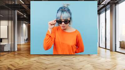 Funny hipster girl with colored hair in sunglasses looks intently at the camera with a serious face. Wall mural