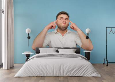 Funny man with a beard shows his fingers on his temple and looks away with a serious face. Wall mural