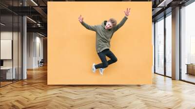 Happy young man jumping against the background of an orange wall. The leap of an emotional student on a bright colored background Wall mural