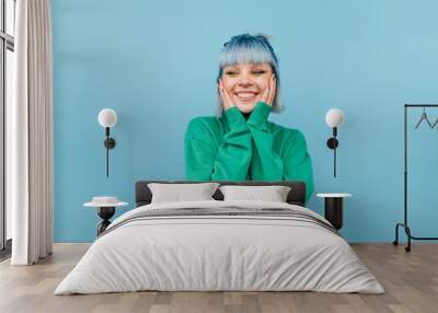 Joyful girl with blue hair stands on a green background with a smile on his face and happy looks away. Wall mural