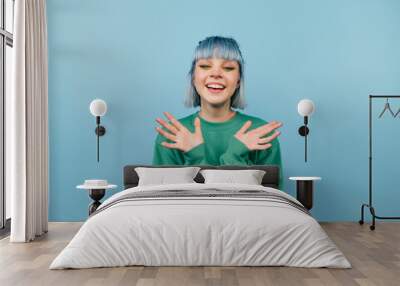 Joyful girl with colored hair stands on a blue background with a happy face looking at the camera Wall mural